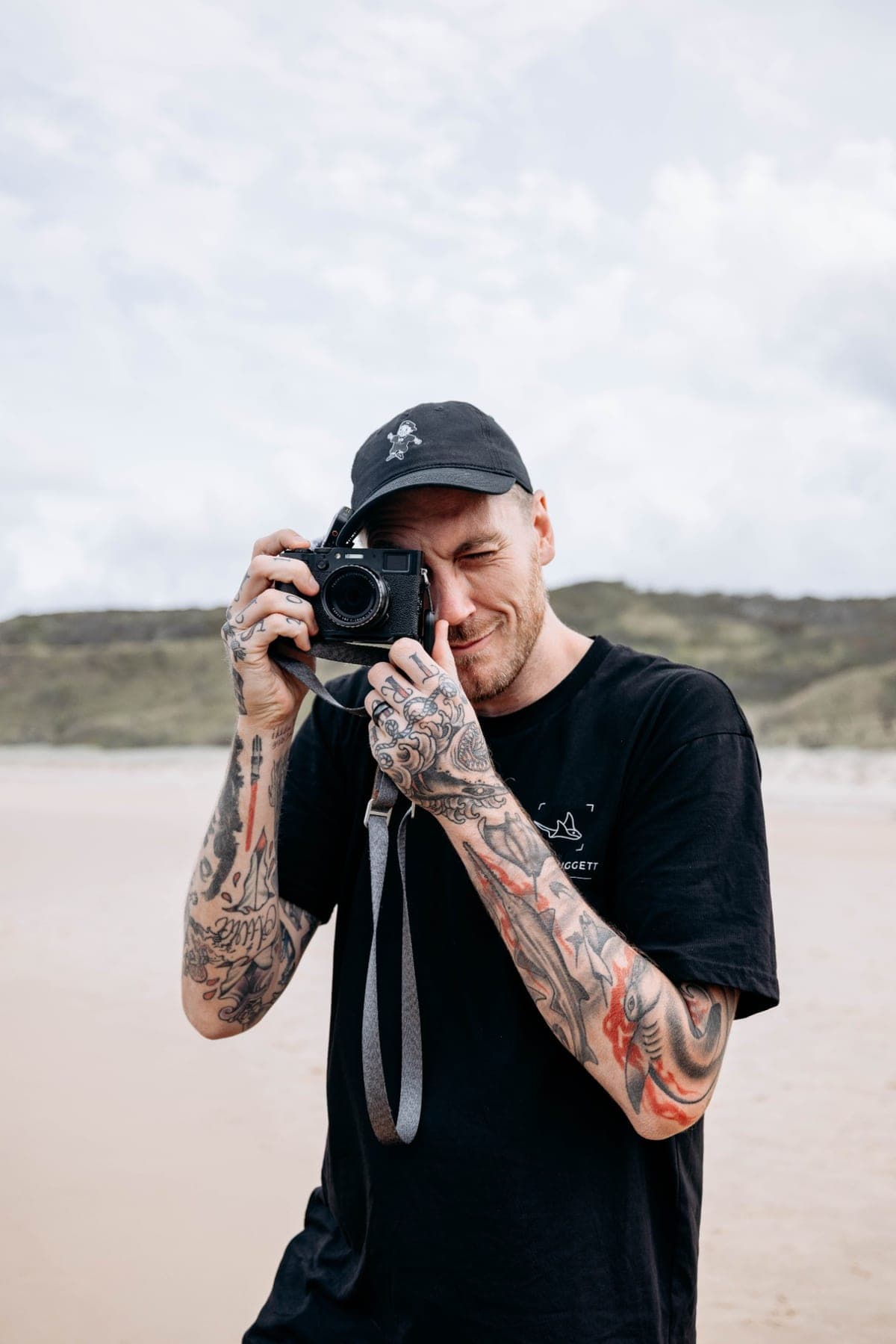 Josh Huggett on a beach, squinting through a small film-style camera
