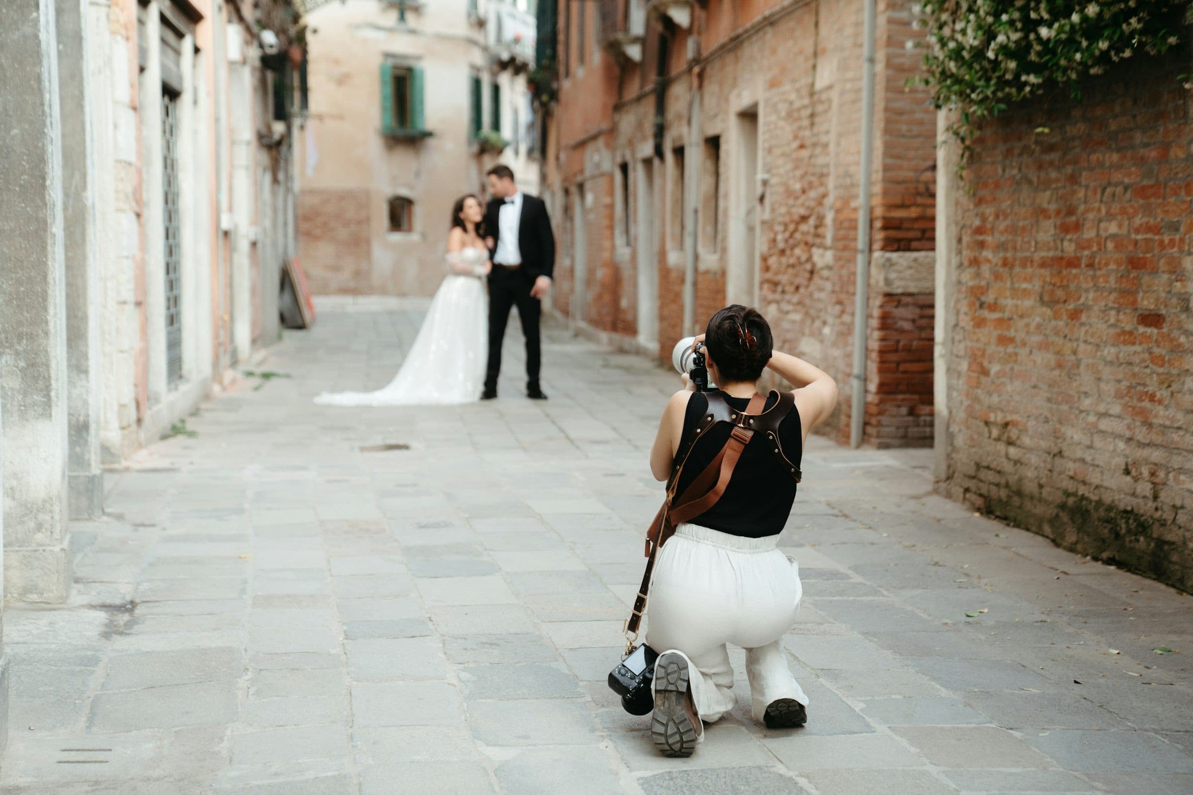 A photographer kneeling in a narrow stone laneway to photograph a bride and groom